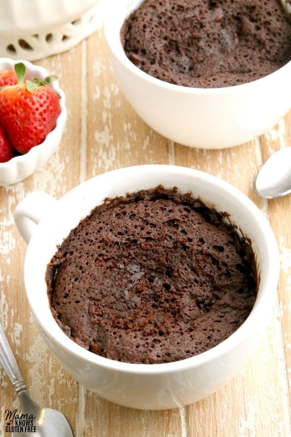 two gluten-free chocolate mug cakes with strawberries in the background