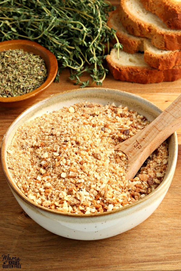 gluten-free bread crumbs in a bowl with a spoon and bread and herbs in the background