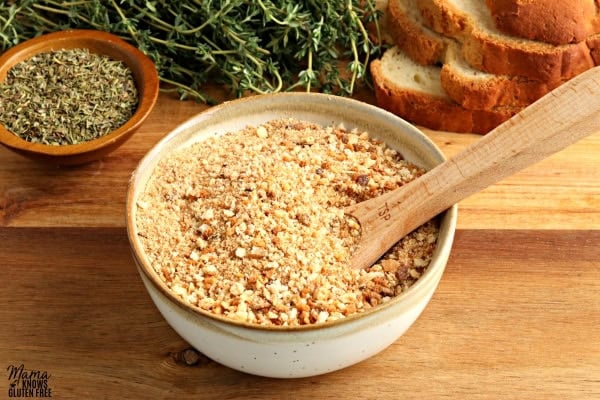 gluten-free bread crumbs in a white bowl with a wooden spoon with herbs and bread slices in the background