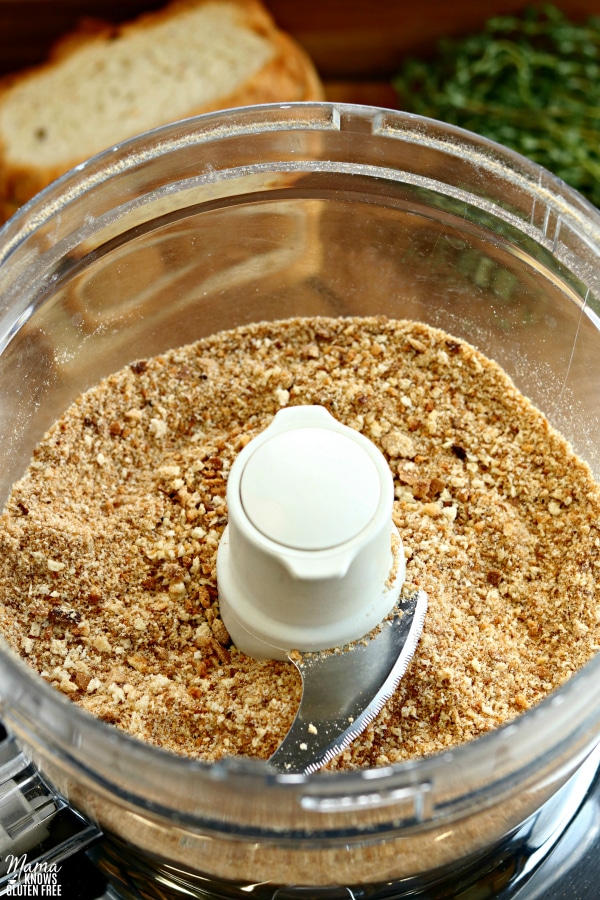 gluten-free bread crumbs in a food processor with bead and herbs in the background