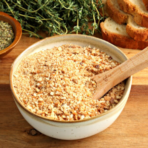 gluten-free bread crumbs in a bowl with a wooden spoon with bread and herbs in the background