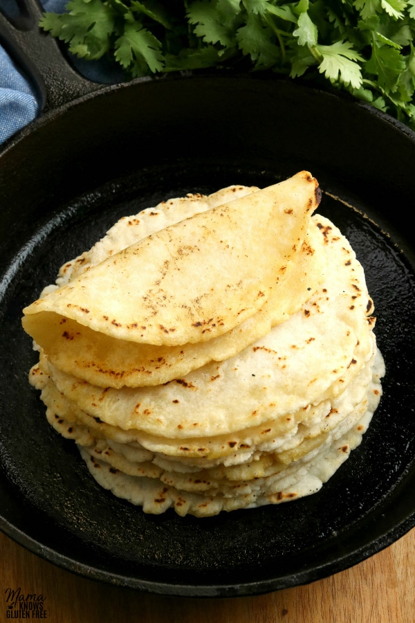 gluten-free tortillas in a cast iron pan with cilantro in the background