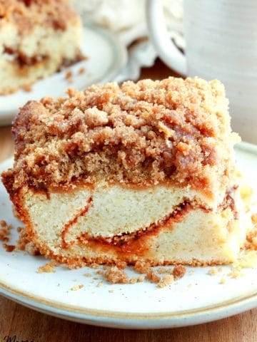 gluten-free coffee cake on a white plate with another slice and coffee in the background