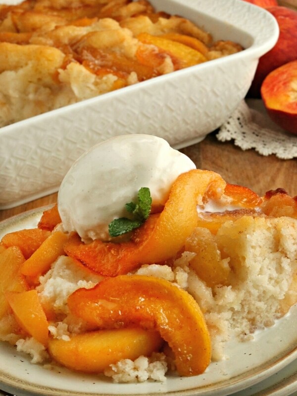 gluten-free peach cobbler with ice cream on a plate with the cobbler in the background