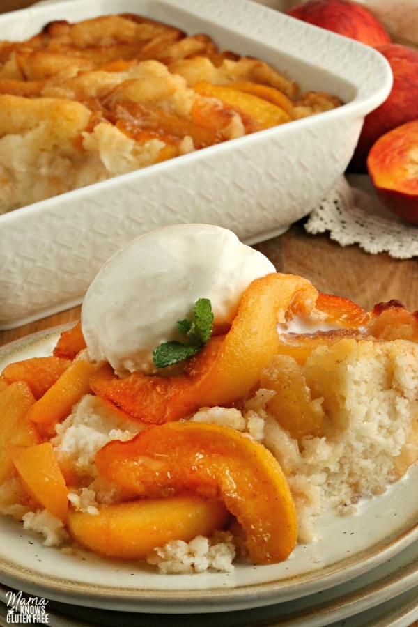 gluten-free peach cobbler with ice cream on a plate with the cobbler in the background
