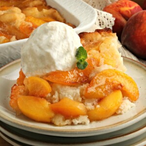 gluten-free peach cobbler topped with vanilla ice cream on a plate with the cobbler and peaches in the background
