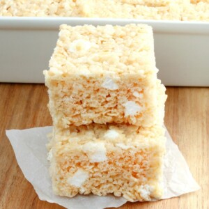2 gluten-free rice krispies treats stacked with the pan of treats in the background