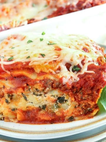 gluten-free lasagna slice on a white plate with the pan of lasagna in the background