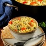 bowl of gluten-free chicken noodle soup with a spoon and crackers with the pot of soup and parsley in the background