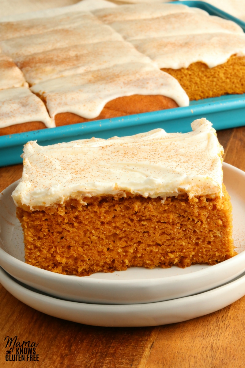 gluten-free pumpkin bar with cream cheese frosting on a white plate with a pan of bars