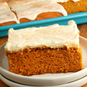 gluten-free pumpkin bars with cream cheese frosting on a white plate with the pan of bars in the background