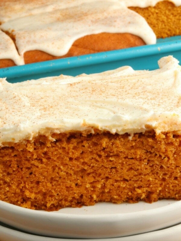 gluten-free pumpkin bars with cream cheese frosting on a white plate with the pan of bars in the background