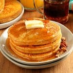 gluten-free pumpkin pancakes topped with butter and syrup on a white plate with more pancakes and syrup in the background