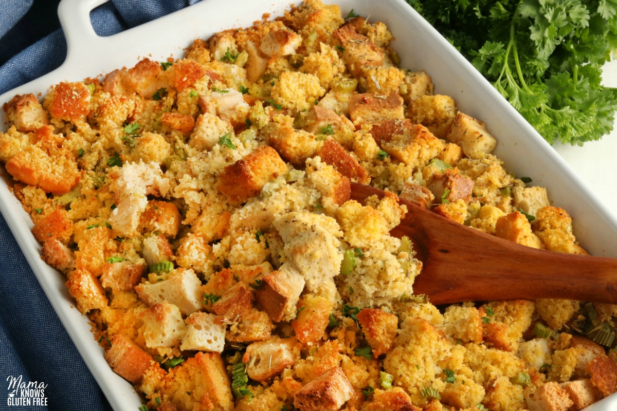 gluten-free cornbread stuffing in a white baking dish and a wooden spoon