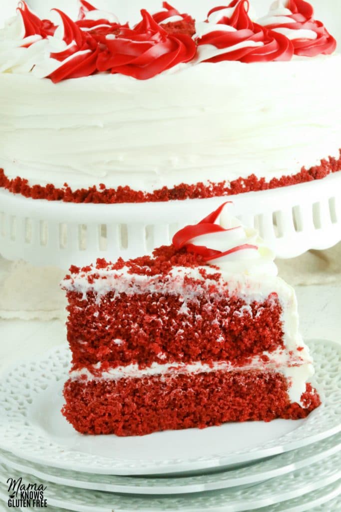 gluten-free red velvet cake slice on a white plate with the cake in the backgorund