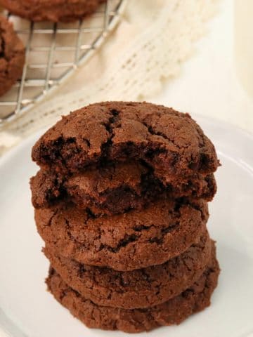 gluten-free chocolate cookies stacked ona white plate with cookies in teh background on a cooling rack