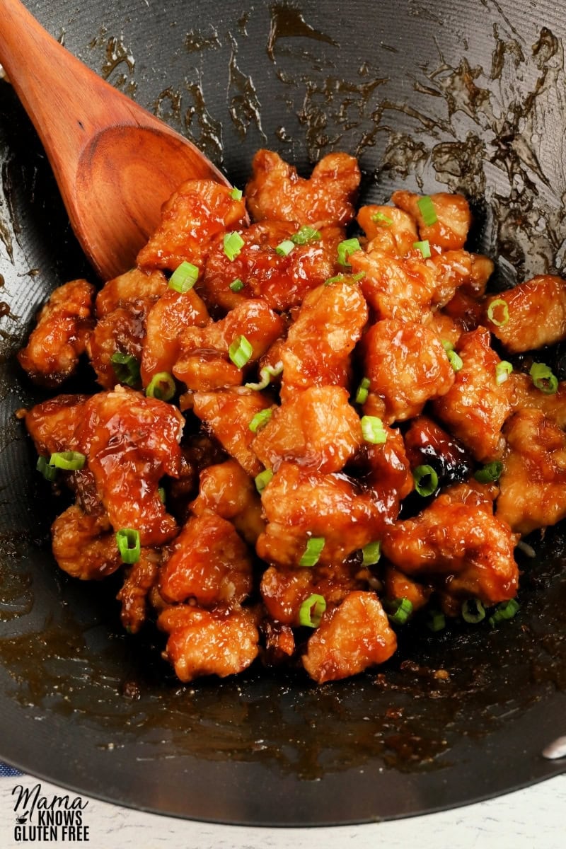 gluten-free orange chicken in a black wok with a wooden spoon