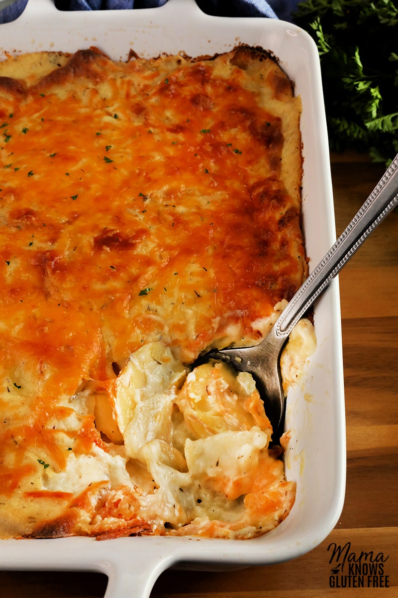 gluten-free scalloped potatoes in a white baking dish with a serving spoon. 