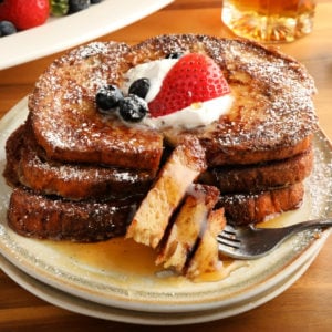 gluten-free French Toast topped with berries, whipped cream, and syrup on a white plate with a fork