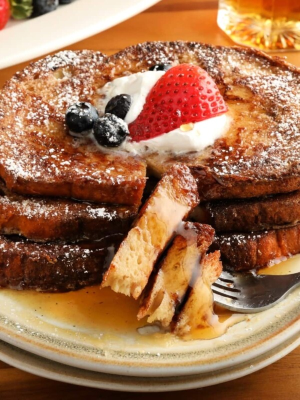 gluten-free French Toast topped with berries, whipped cream, and syrup on a white plate with a fork