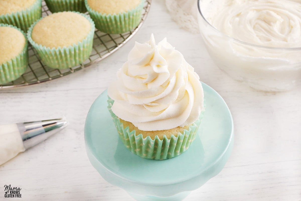 gluten-free vanilla buttercream frosting on a vanilla cupcakes with the frosting and cupcakes in the background