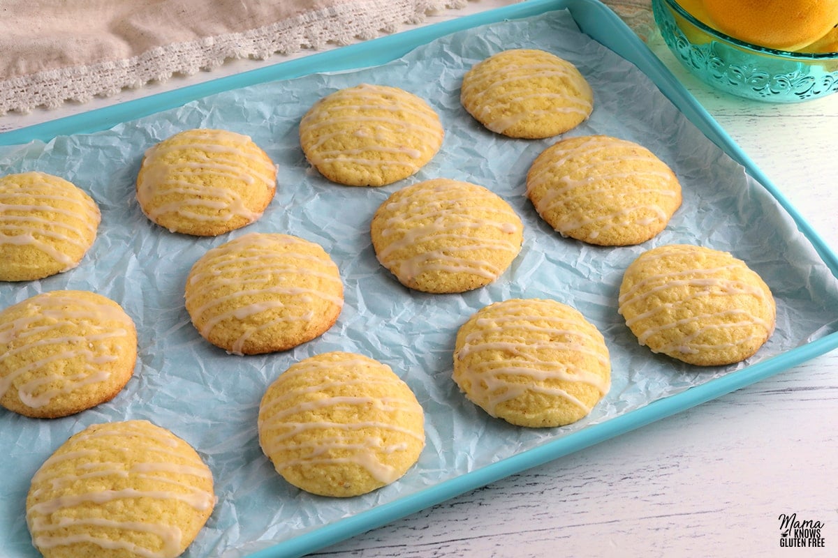 gluten-free lemon cookies on a blue cookie sheet with a bowl of lemons in the background