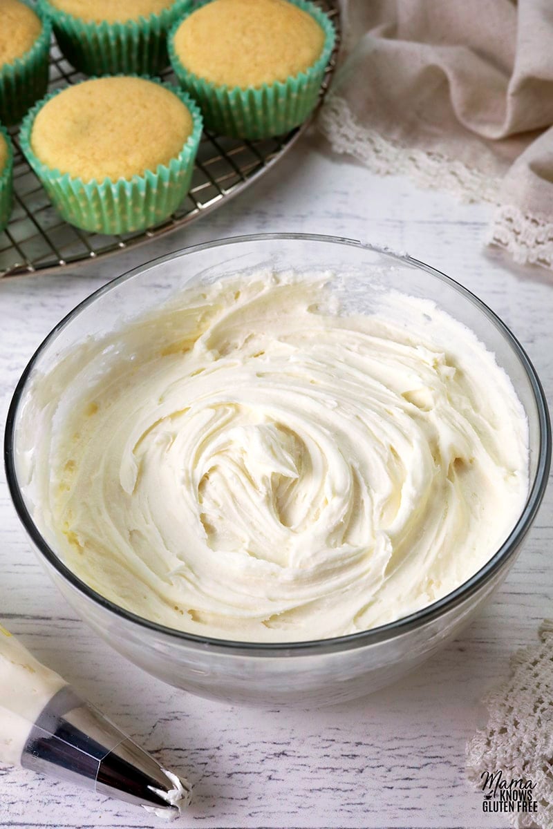 bowl of gluten-free frosting with a frosting piping bag, vanilla cupcakes in the background