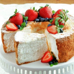 gluten-free and dairy-free angel food cake topped with berries on a white cake stand