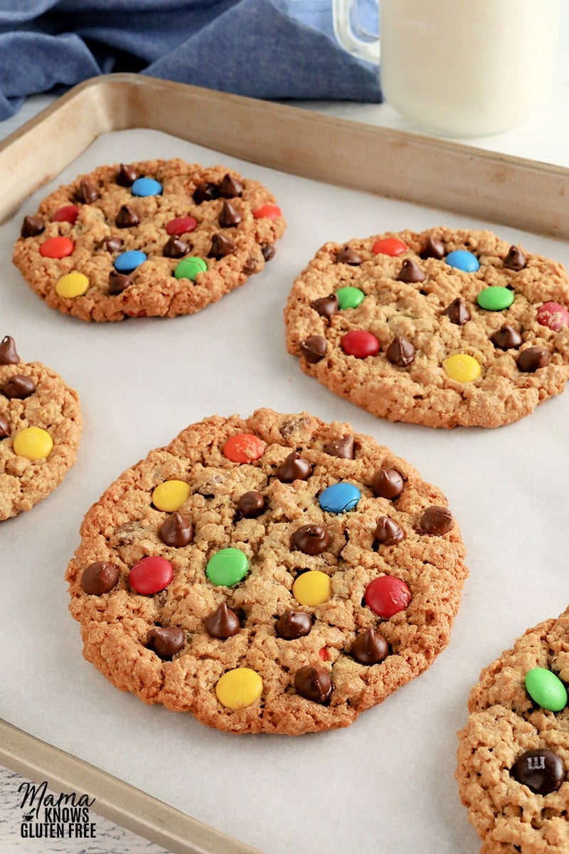 gluten-free monster cookies on a baking sheet with a glass of milk in the background