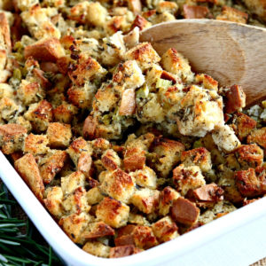 gluten-free stuffing in a white baking dish with a wooden spoon and fresh rosemary