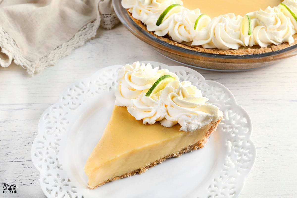 slice of gluten-free key lime pie topped with whipped cream on a plate with the pie in the background