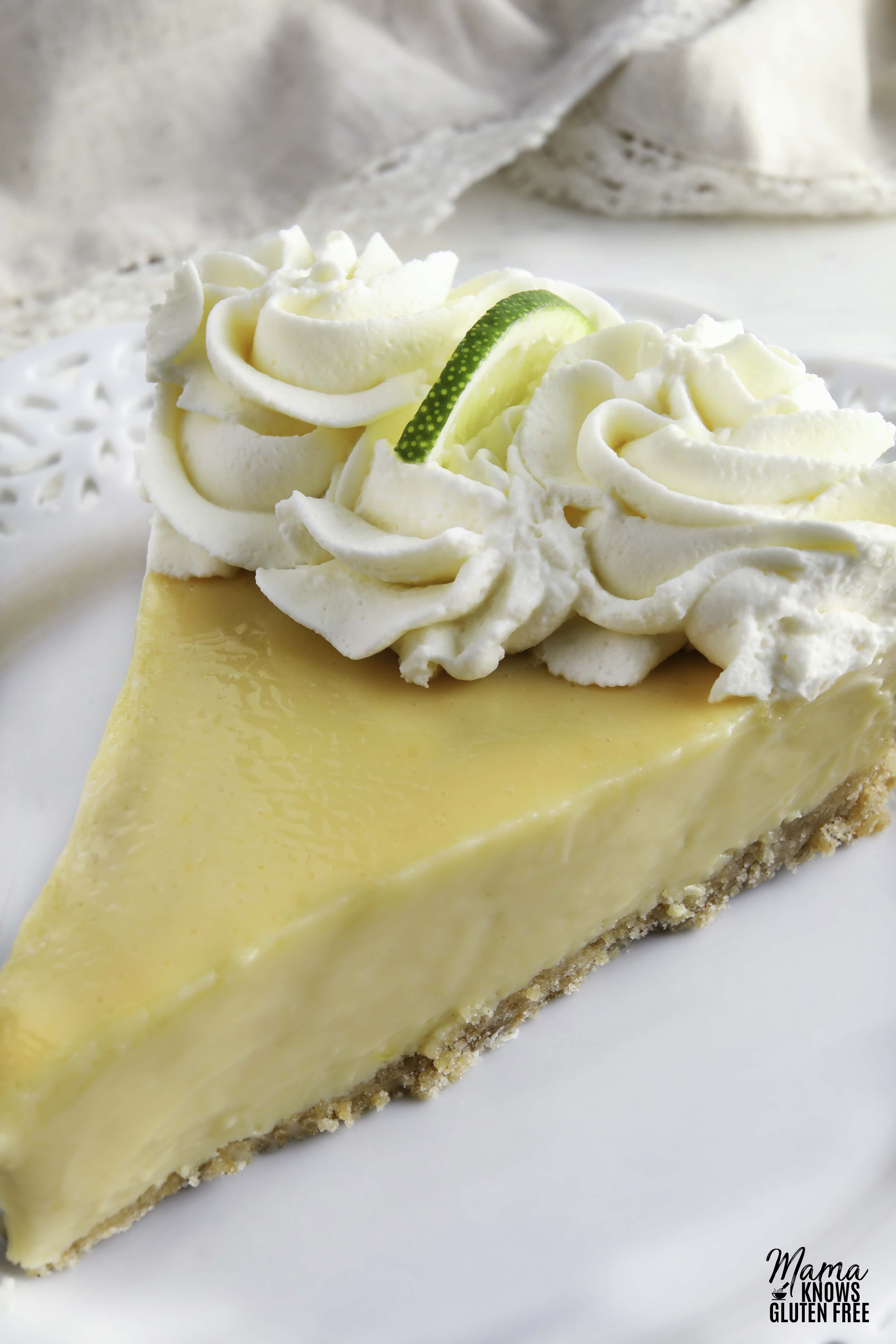 close up photo of a slice of gluten-free key lime pie slice topped with whipped cream and a lime slice on a white plate