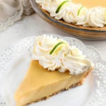 gluten-free key lime pie slice topped with whipped cream on a white plate with the pie in the background