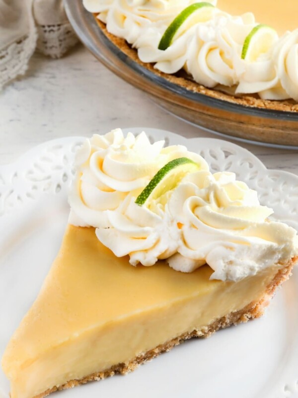 gluten-free key lime pie slice topped with whipped cream on a white plate with the pie in the background