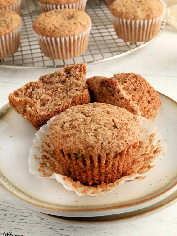 two gluten-free zucchini muffins on white plate with a cooling rack with the muffins in the background