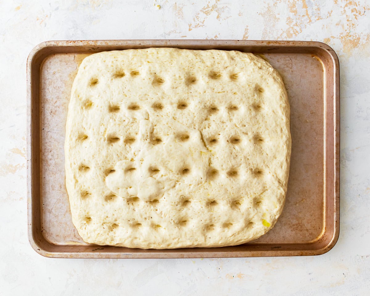 dimpled gluten-free focaccia dough on a baking sheet.