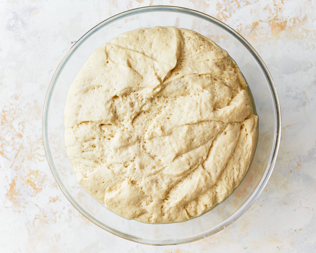 risen gluten-free focaccia dough in a glass bowl.