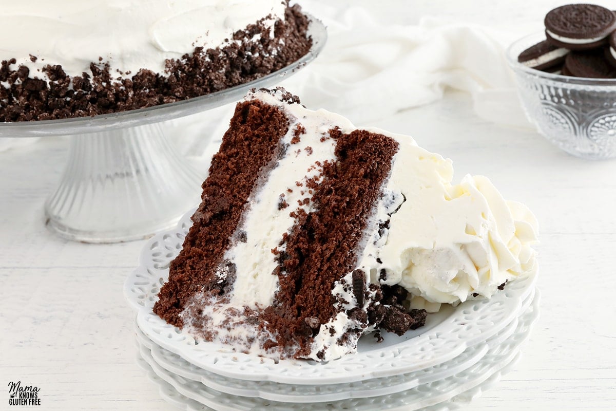 gluten-free ice cream cake slice on a white plate with the cake and chocolate cookies in the background