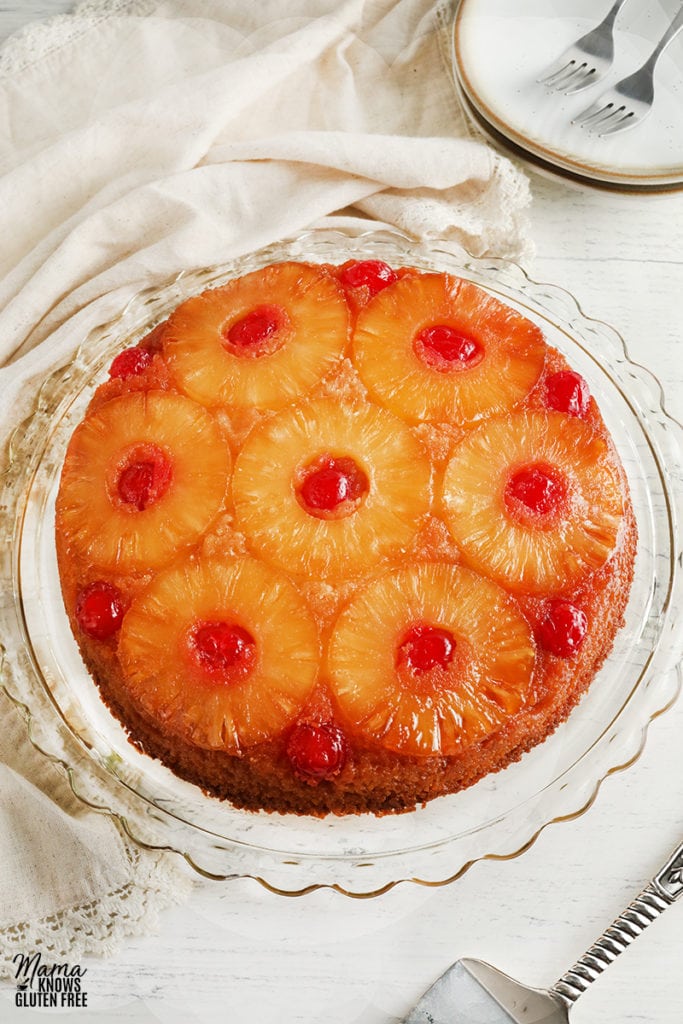 gluten-free pineapple upside down cake on a cake plate with plates and cake cutter in the background