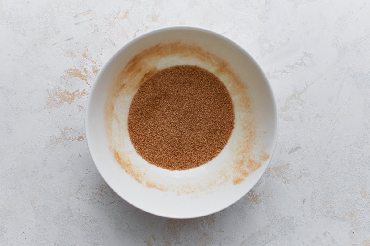 A white bowl filled with a mixture of granulated sugar and ground cinnamon, ready for coating gluten-free snickerdoodle cookie dough.