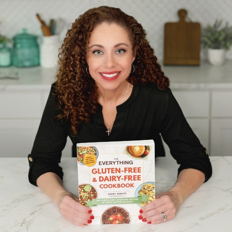 Audrey Roberts holding The Everything Gluten Free & Dairy Free Cookbook in a white kitchen