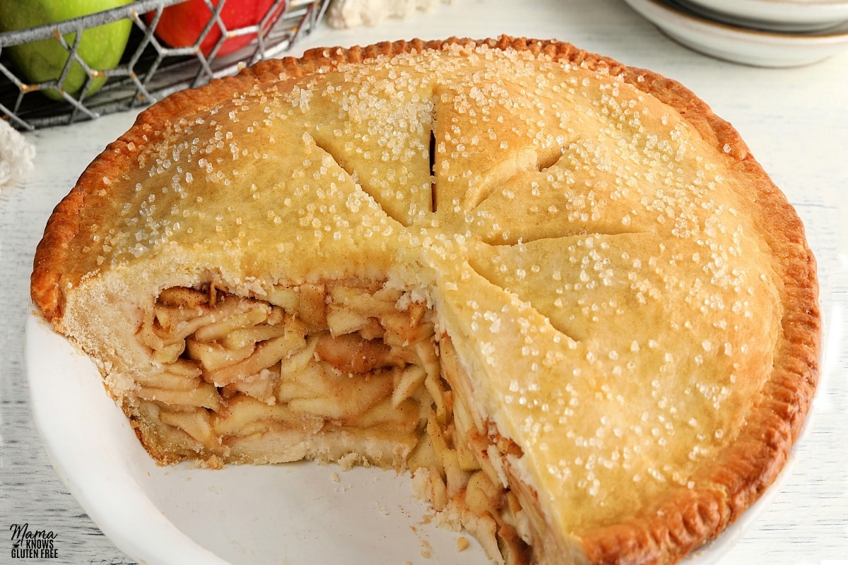 gluten-free apple pie with a slice cut out with apples in the background