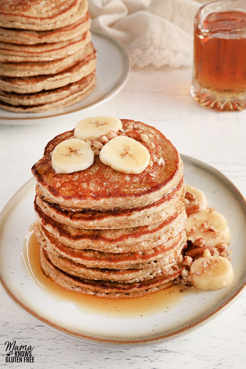 banana oatmeal pancakes stacked on a white plate with sliced bananas and syrup