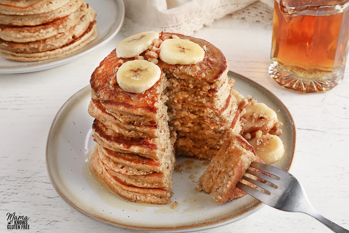 banana oatmeal pancakes cut to show fluffy texture on a white plate with sliced bananas and syrup