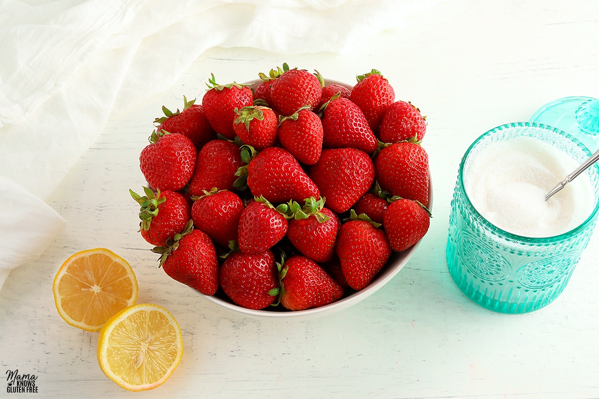 strawberries in a white bowl with ateal sugar jar and sliced lemon
