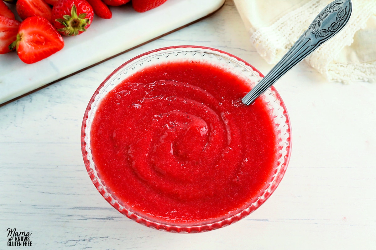 strawberry reduction sauce in a glass bowl with a spoon and strawberries in the background