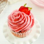strawberry frosting piped on a strawberry cupcake topped with a sliced strawberry