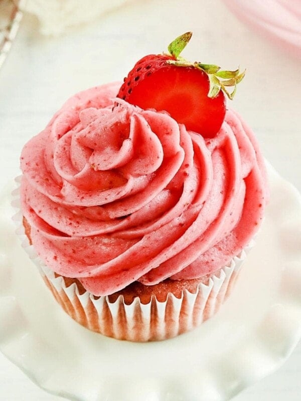 strawberry frosting piped on a strawberry cupcake topped with a sliced strawberry