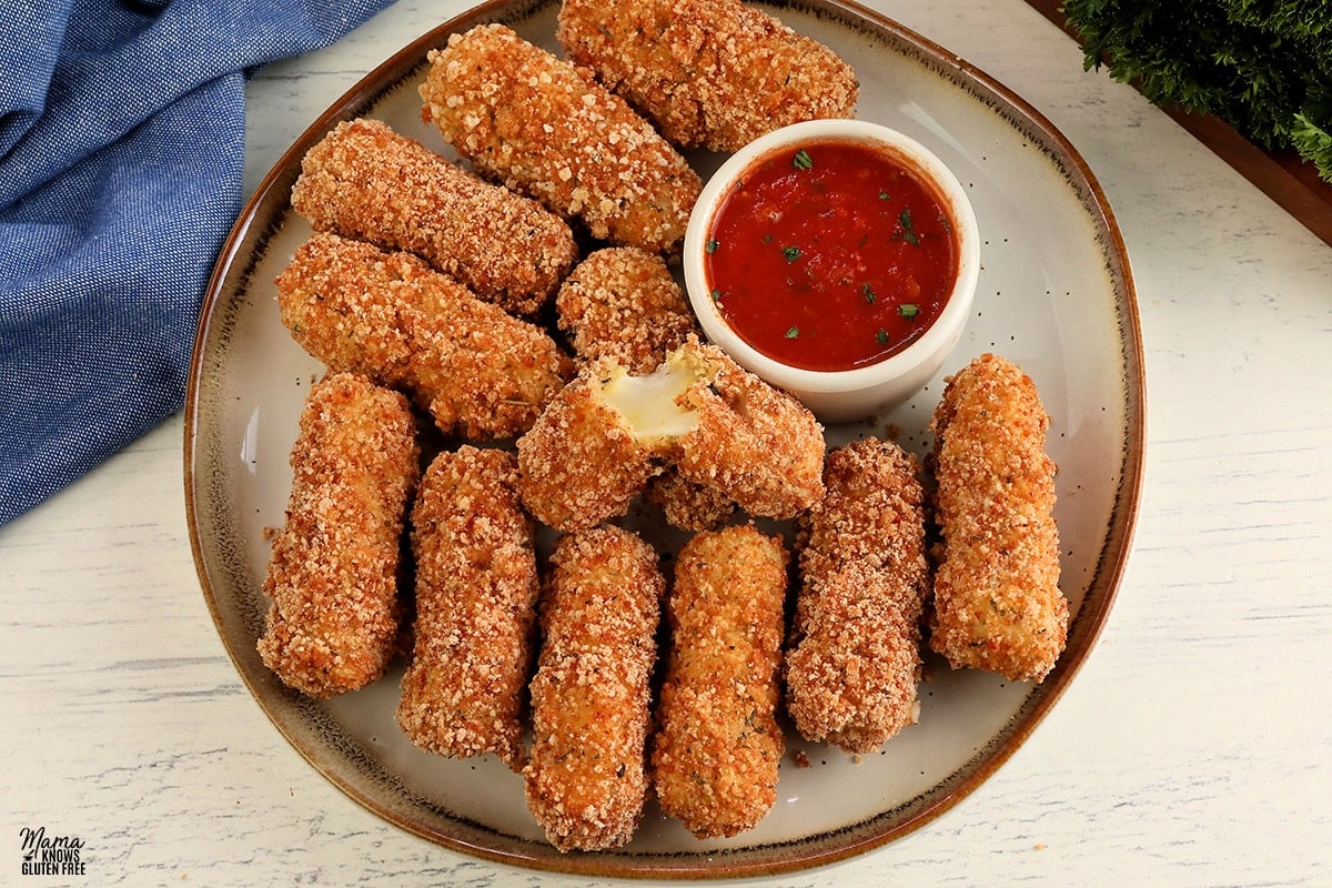 gluten-free mozzarella sticks on a white plate with one broken open to see the melted cheese