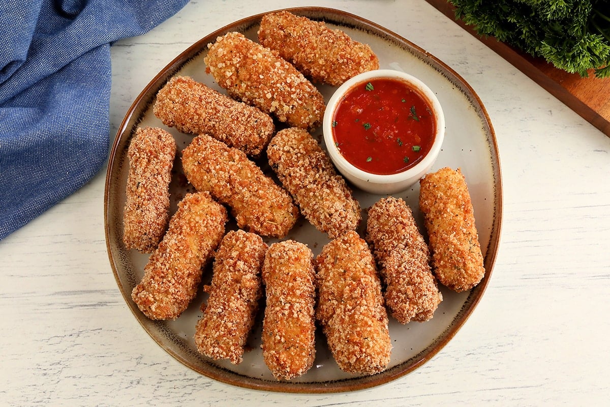 gluten-free mozzarella sticks on a white plate with a side of marinara sauce